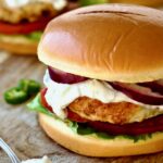 Ground Chicken Burgers with Spicy Tzatziki on wood cutting board with spoon of tzatziki next to it.