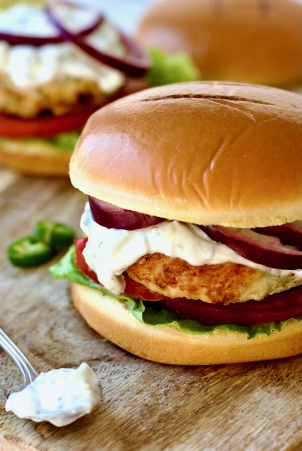Ground Chicken Burgers with Spicy Tzatziki on wood cutting board with spoon of tzatziki next to it.