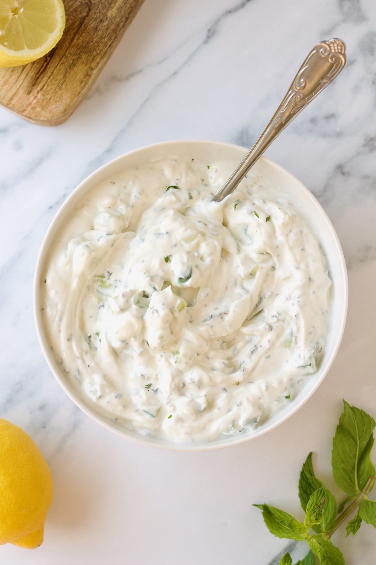 Tzatziki in white bowl with ornate spoon on marble countertop.