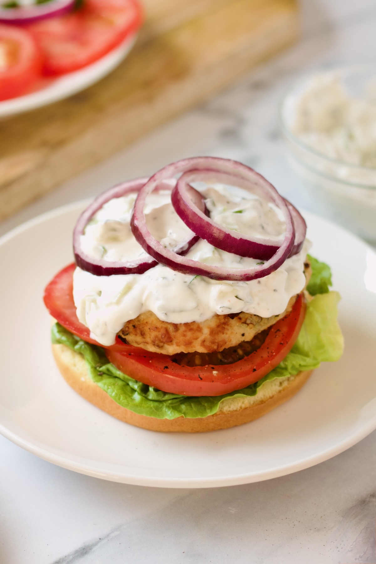 Ground Chicken Burgers with Spicy Tzatziki on white plate before bun is placed on top.