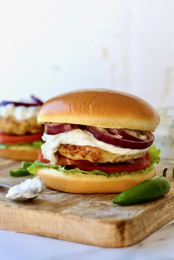 Ground Chicken Burgers with Spicy Tzatziki on wood cutting board with tzatziki on spoon and jalapeno next to the burger.