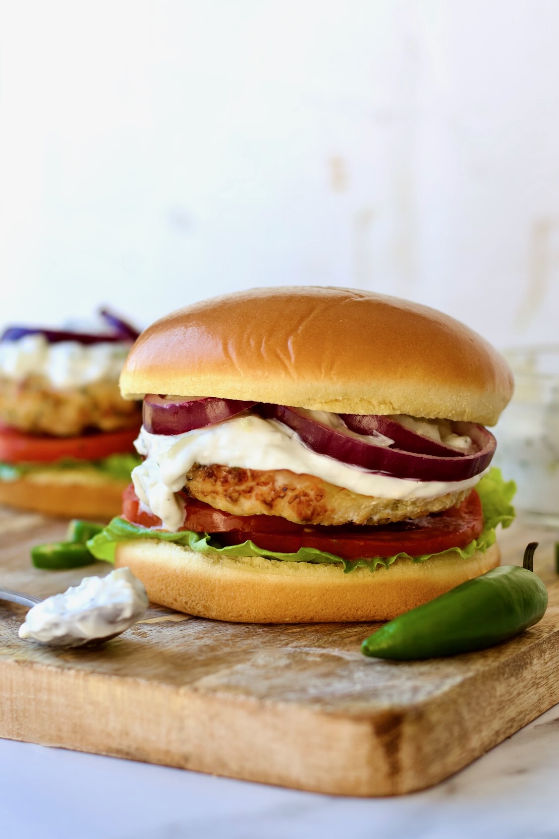 Ground Chicken Burgers with Spicy Tzatziki on wood cutting board with tzatziki on spoon and jalapeno next to the burger.