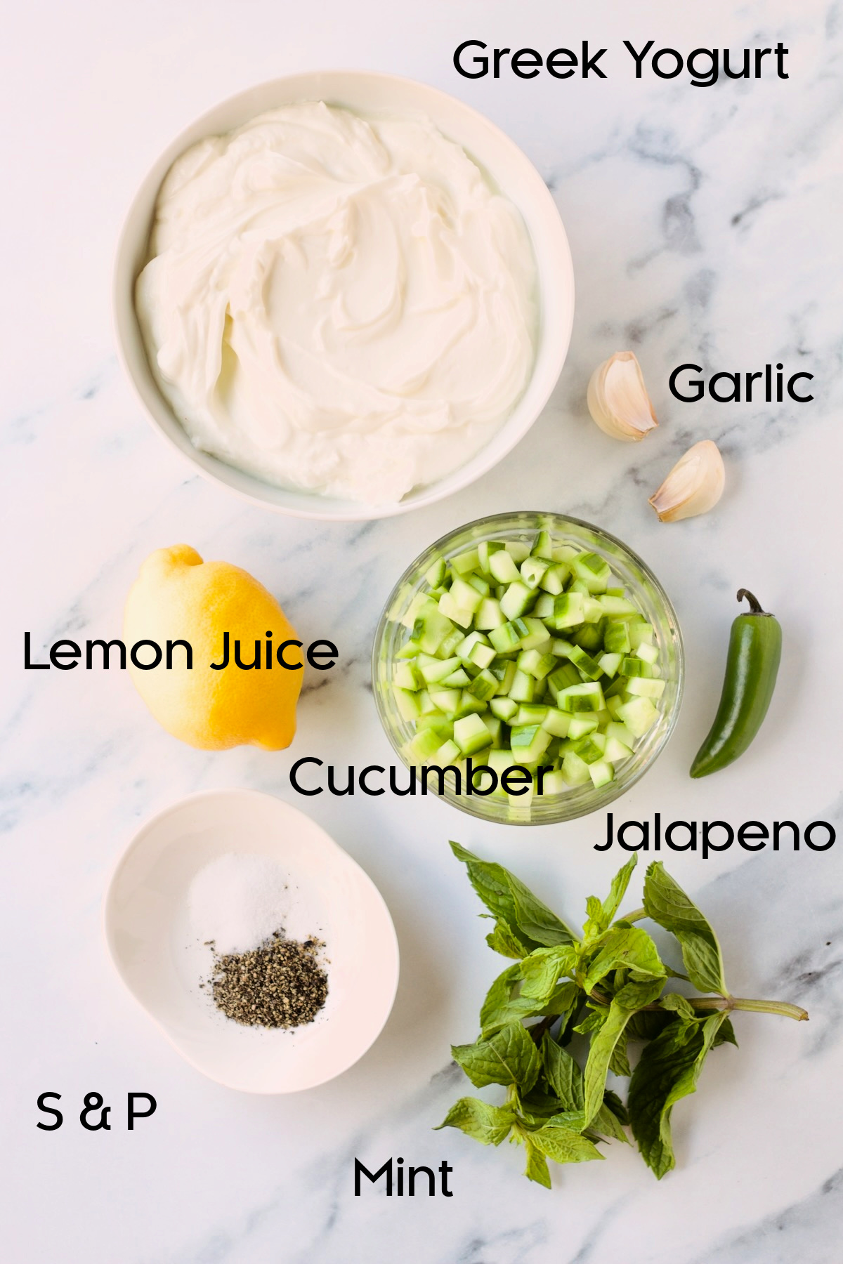 Ingredients for Spicy Tzatziki in bowls on marble countertop.