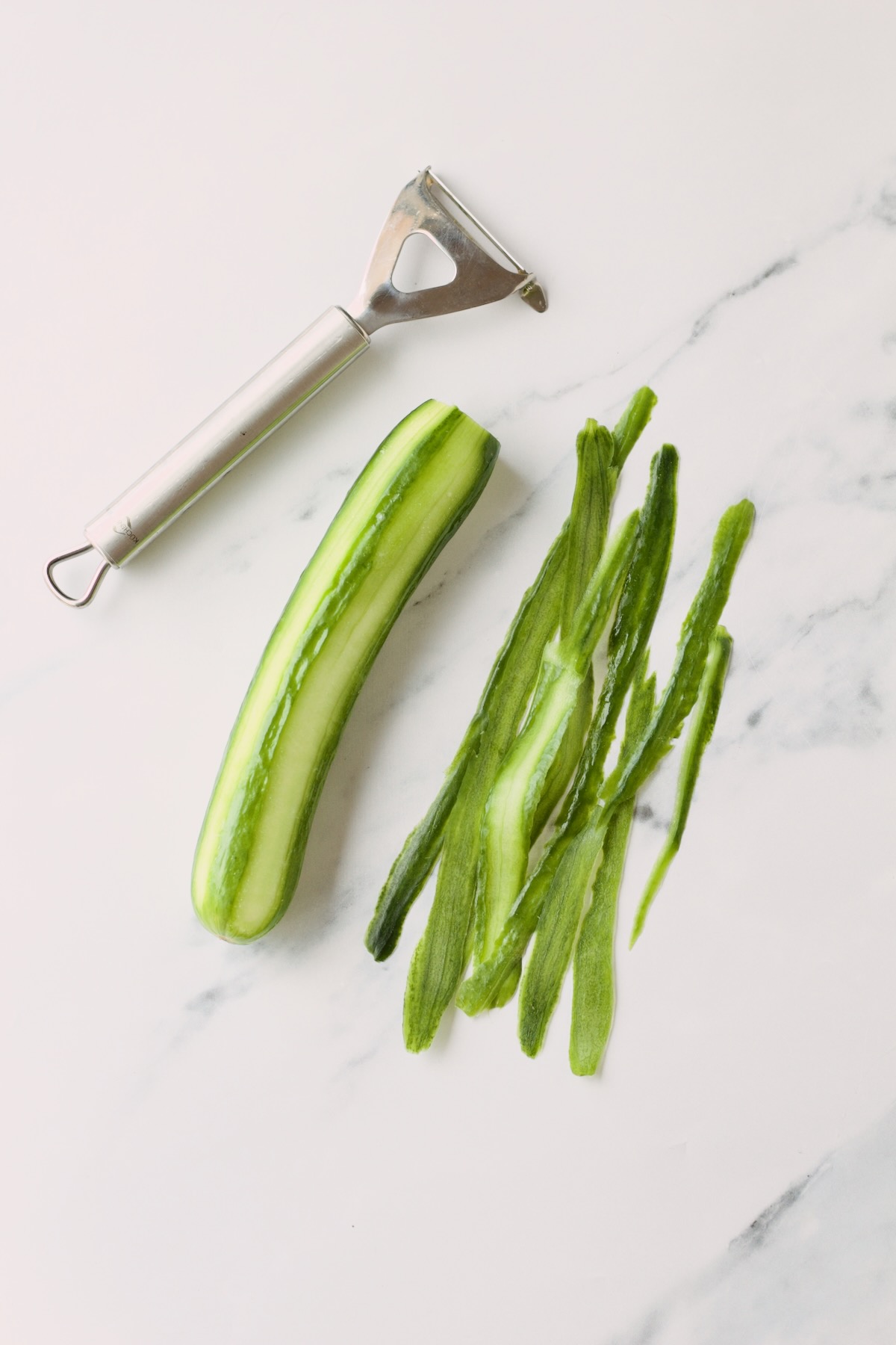 Semi-peeled cucumber with vegetable peeler on countertop.