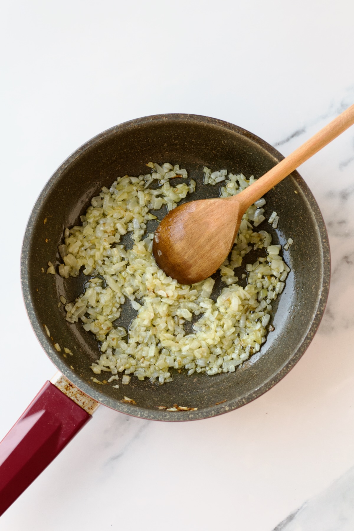 Onions being sauteed with wooden spoon in nonstick skillet.