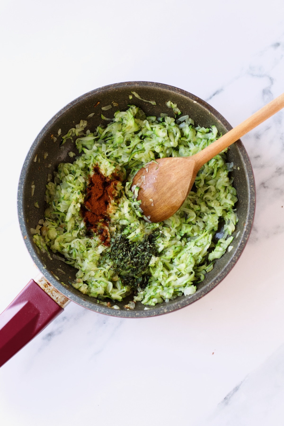Cayenne and oregano added to sauteed zucchini and onions in nonstick skillet with wooden spoon.