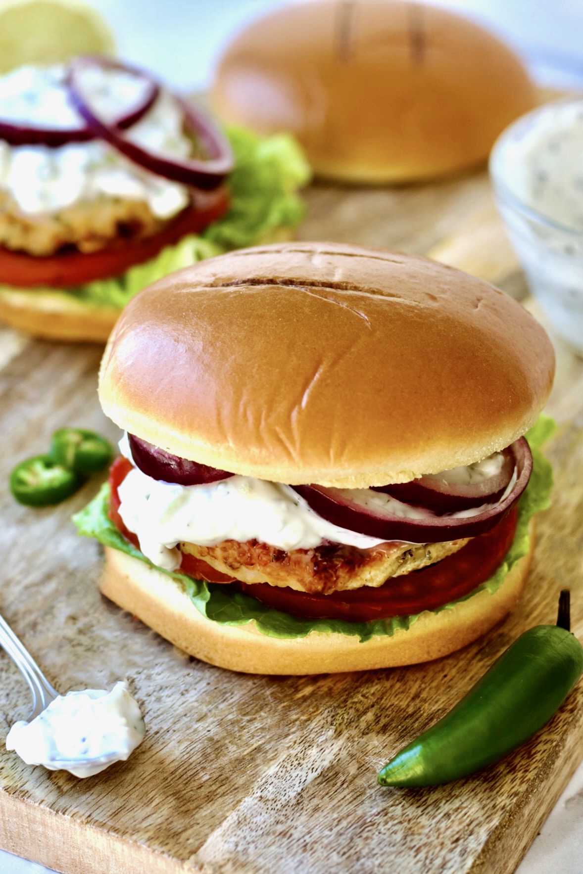 Ground Chicken Burgers with Spicy Tzatziki on wood cutting board.
