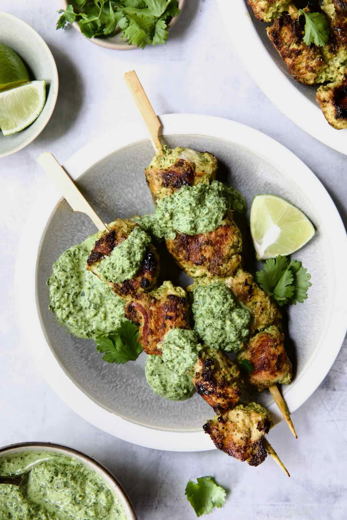 Two Yogurt Marinated Grilled Chicken Skewers with Cilantro Mint Chutney on white and gray plate.