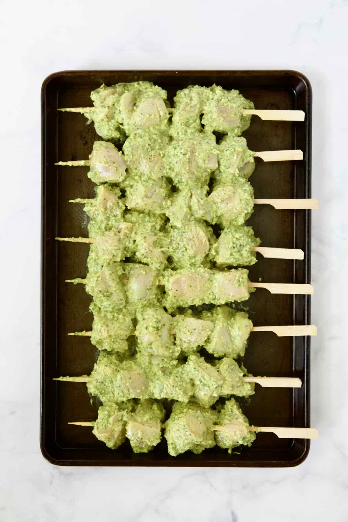 Eight uncooked chicken skewers on rimmed sheet pan.