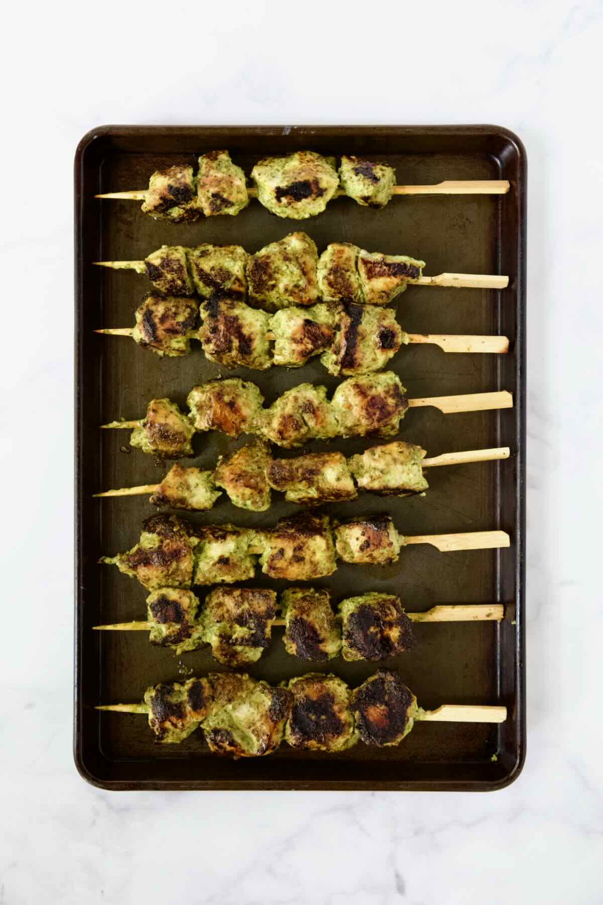Eight grilled chicken skewers on rimmed sheet pan.