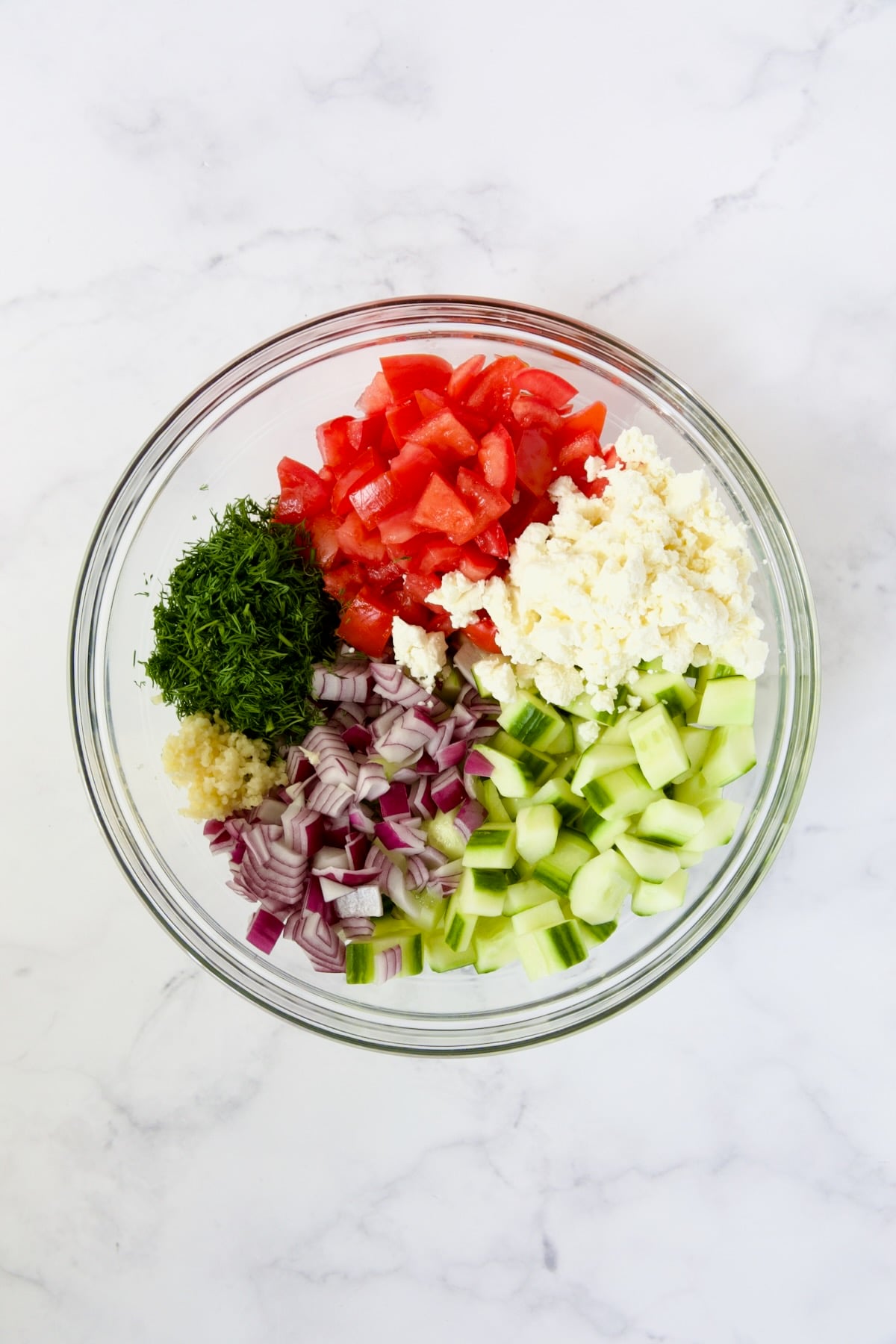 Ingredients for Cucumber Tomato Feta Salad in glass bowl before being mixed together.