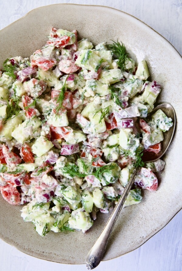 Cucumber Tomato Feta Salad in round ceramic bowl with serving spoon.
