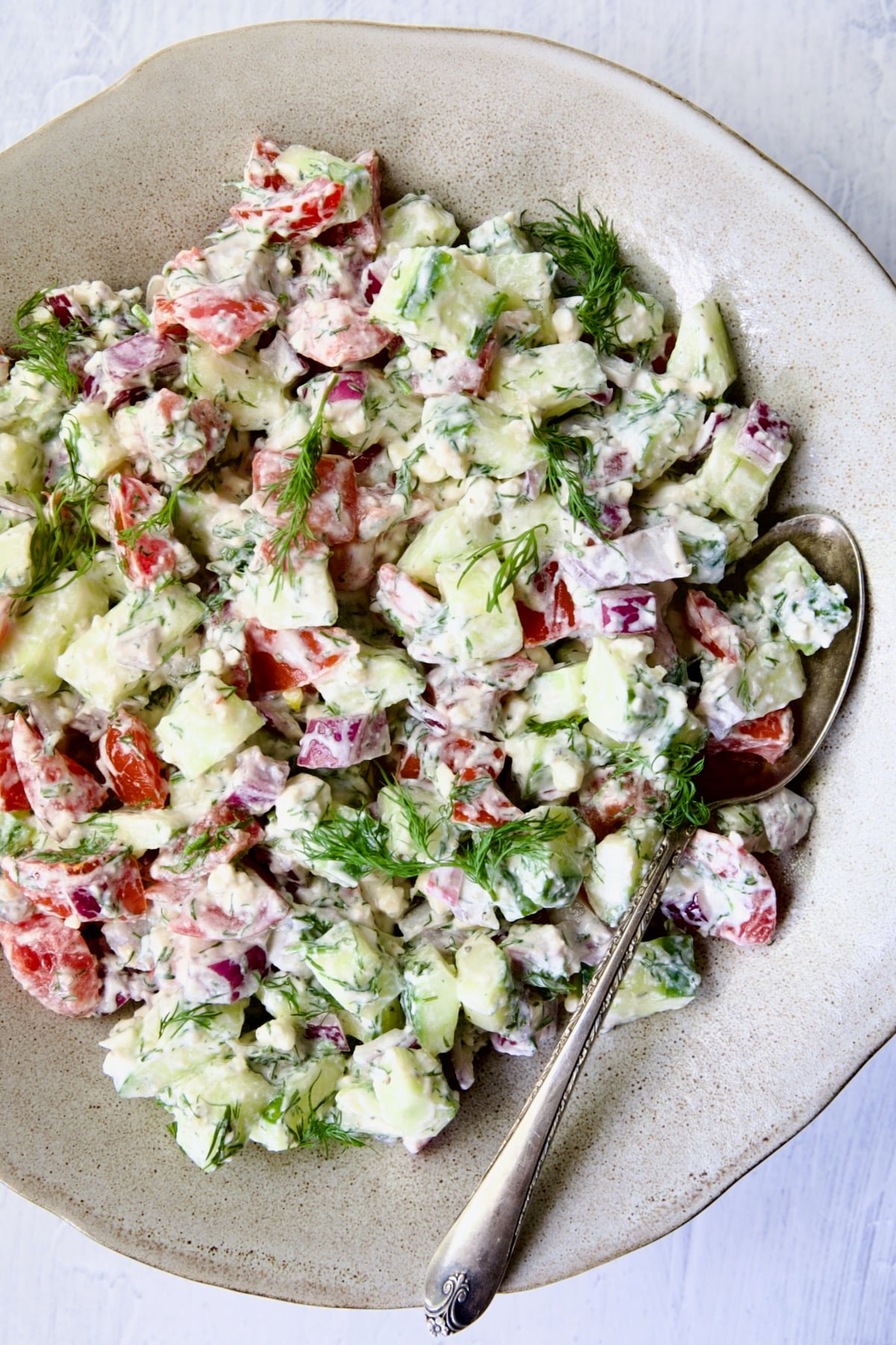 Cucumber Tomato Feta Salad in round ceramic bowl with serving spoon.