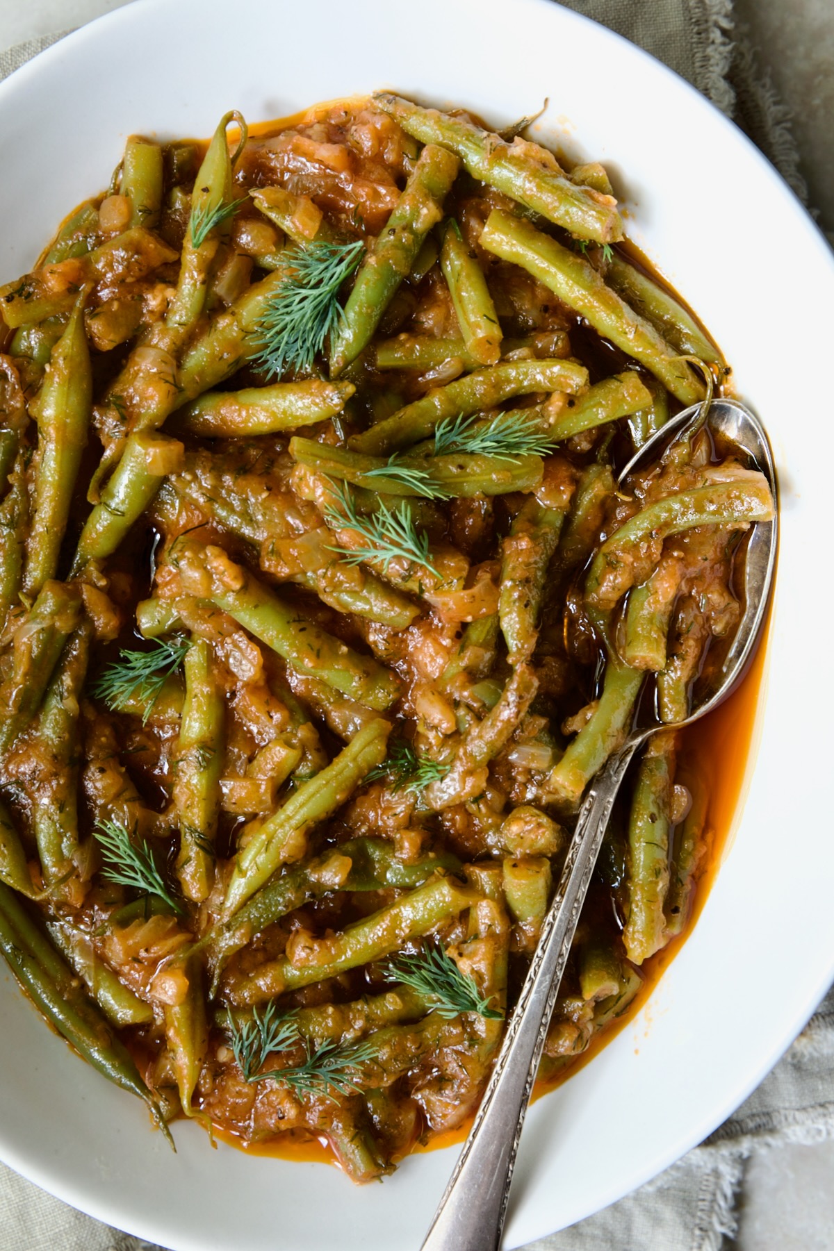 Greek Green Beans in white serving bowl with serving spoon garnished with fresh dill.