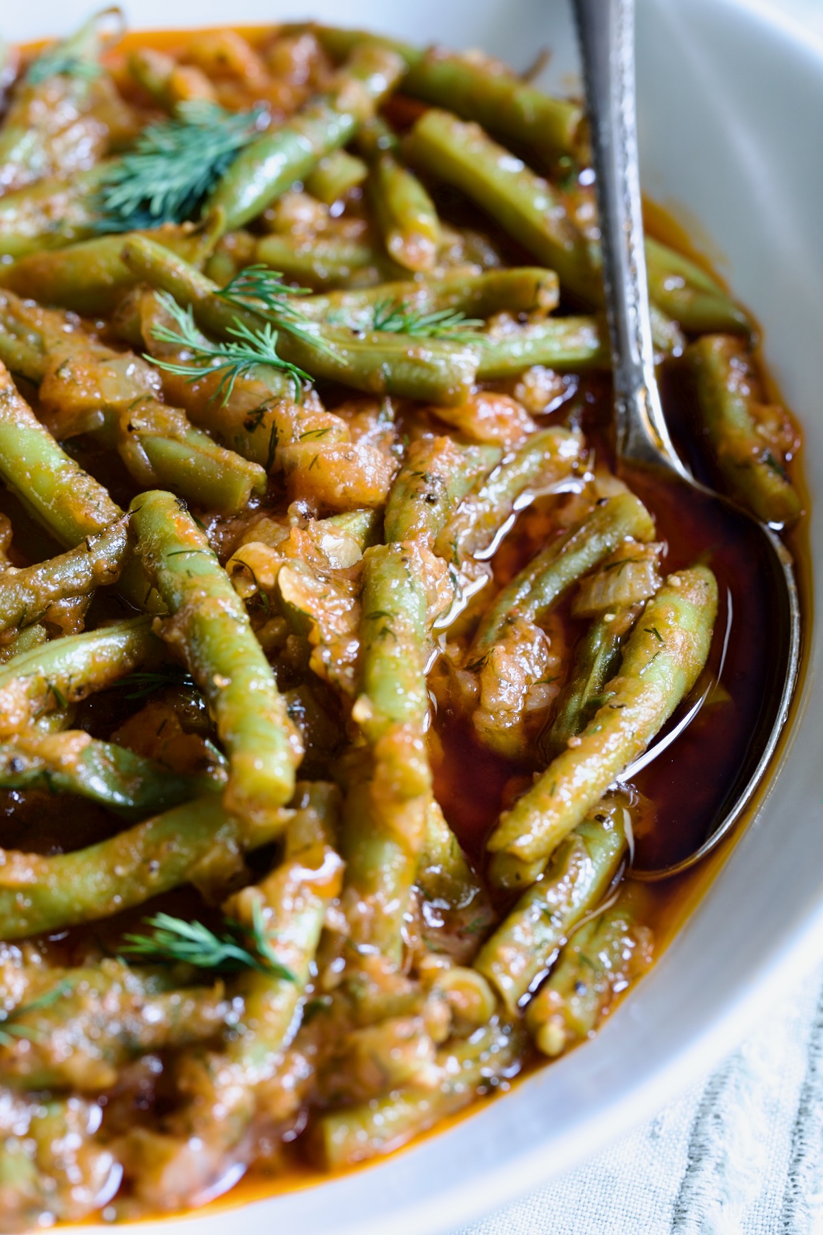 Greek Green Beans in white bowl with serving spoon.