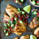 Grilled Tilapia with Tomato - Avocado Salsa with lime wedges on sheet pan.