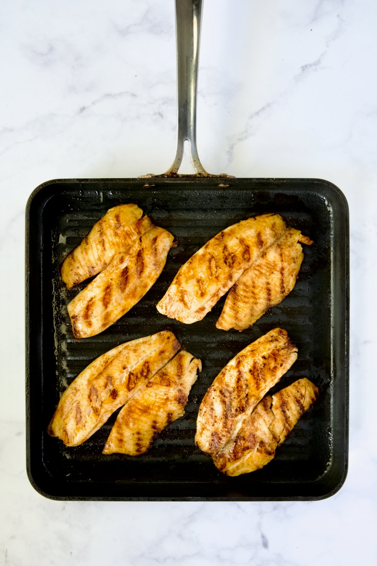 Four pieces of grilled tilapia on nonstick square grill pan.