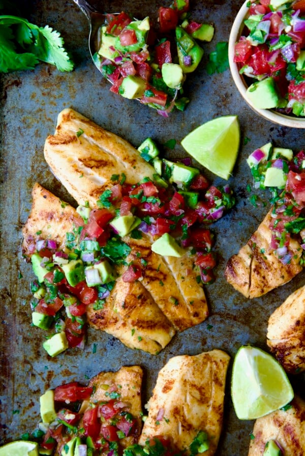 Grilled Tilapia with Tomato - Avocado Salsa with lime wedges on sheet pan.