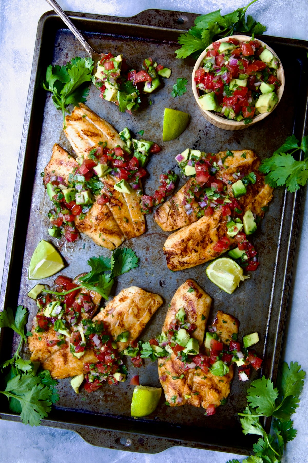 Four pieces of Grilled Tilapia with Tomato - Avocado Salsa on sheet pan.