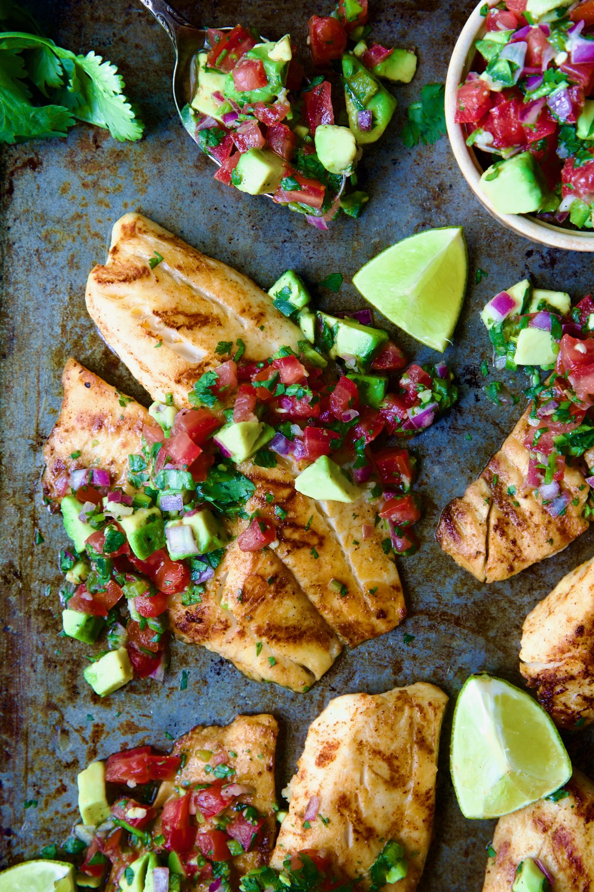 Grilled Tilapia with Tomato - Avocado Salsa with lime wedges on sheet pan.