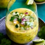 Mango Gazpacho on metal tray garnished with cilantro and lime wedges.