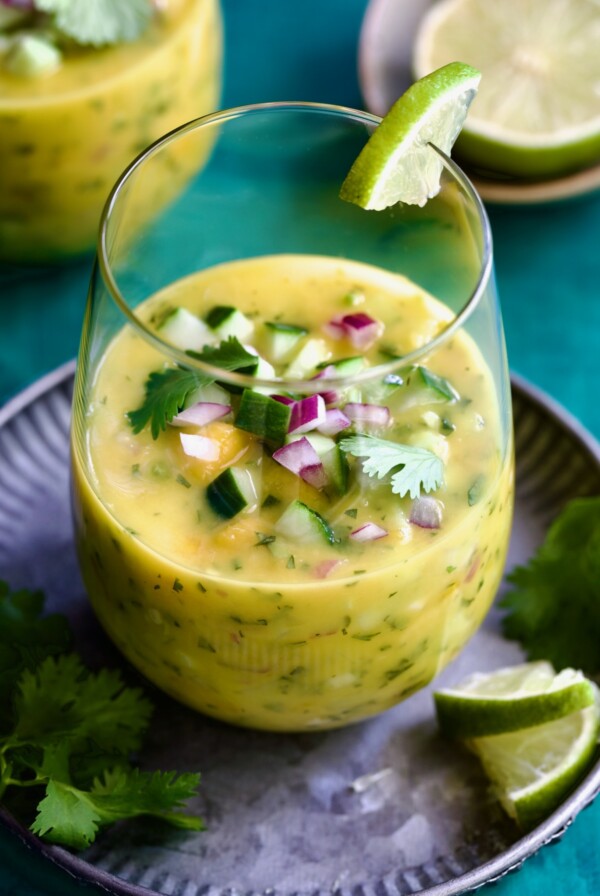 Mango Gazpacho on metal tray garnished with cilantro and lime wedges.