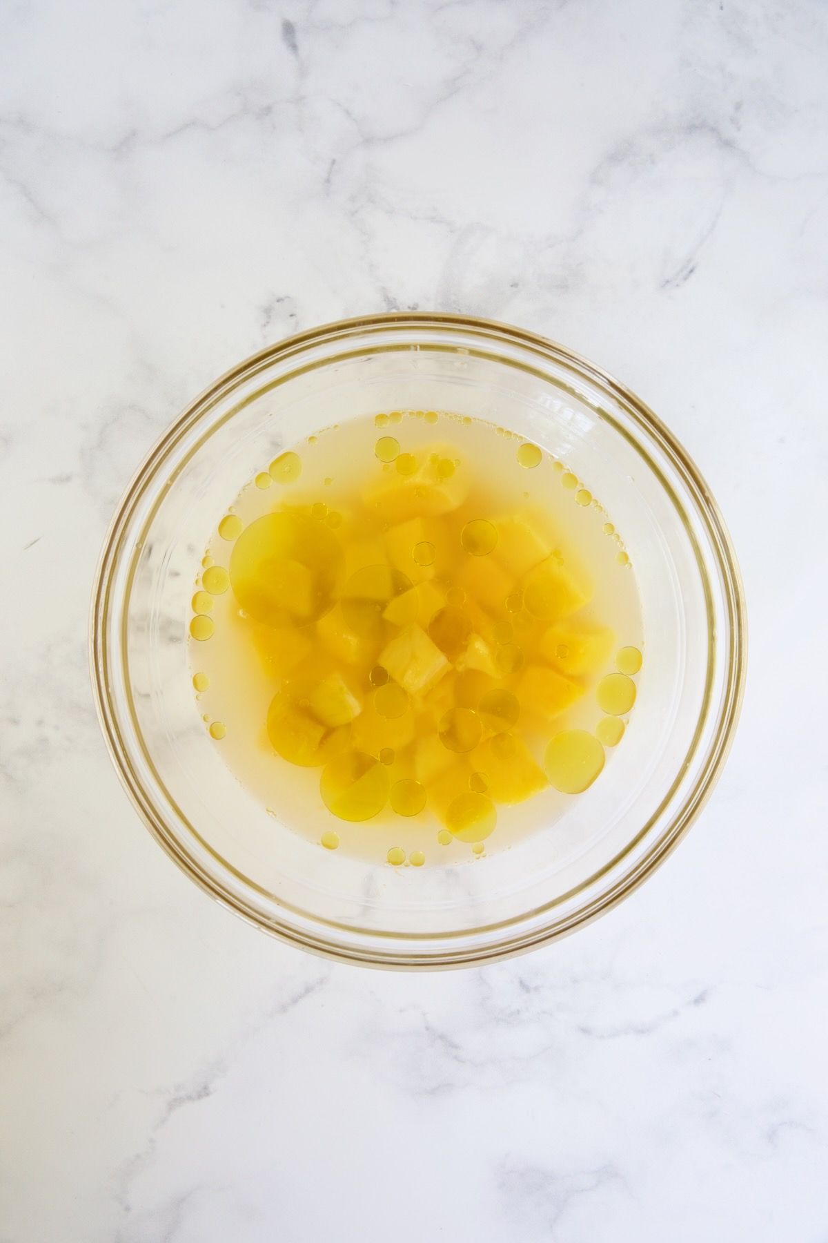 Mango chunks in water, rice vinegar, lime juice and olive oil in glass bowl.