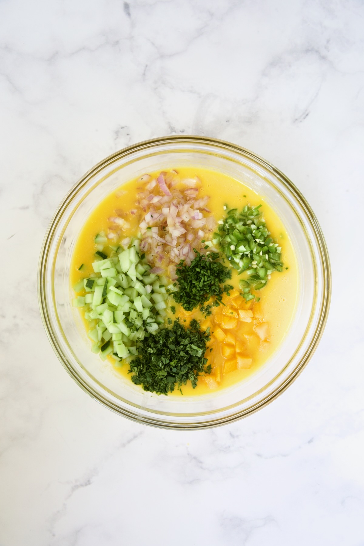 Cucumber, red onion, serranos, fresh mango, chives and cilantro in mango puree in glass bowl.