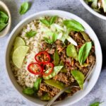 Thai Basil Beef in white bowl garnished with lime wedges, fresh basil and Fresno chiles.