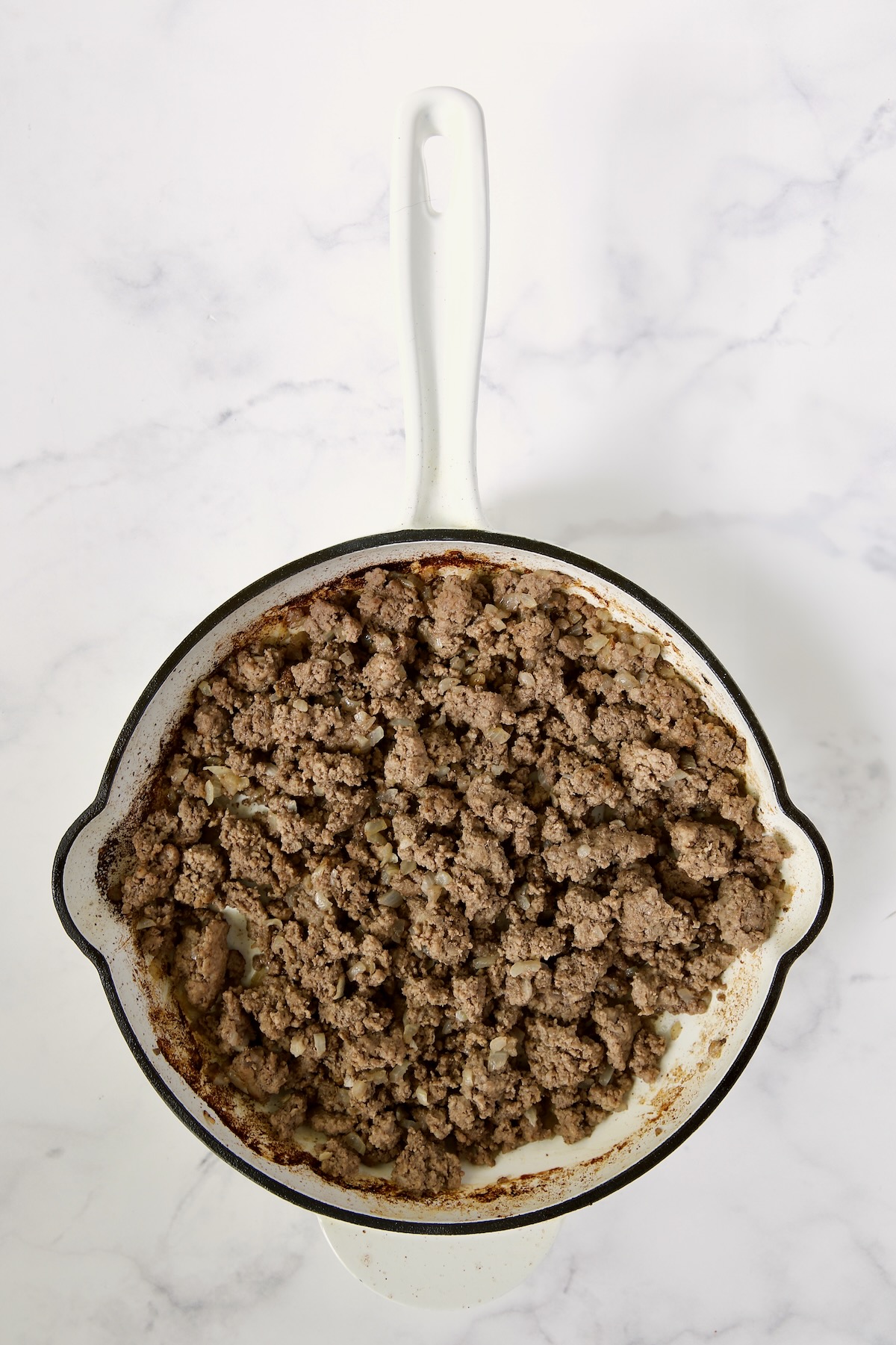 Cooked ground beef in white enamel cast iron skillet.