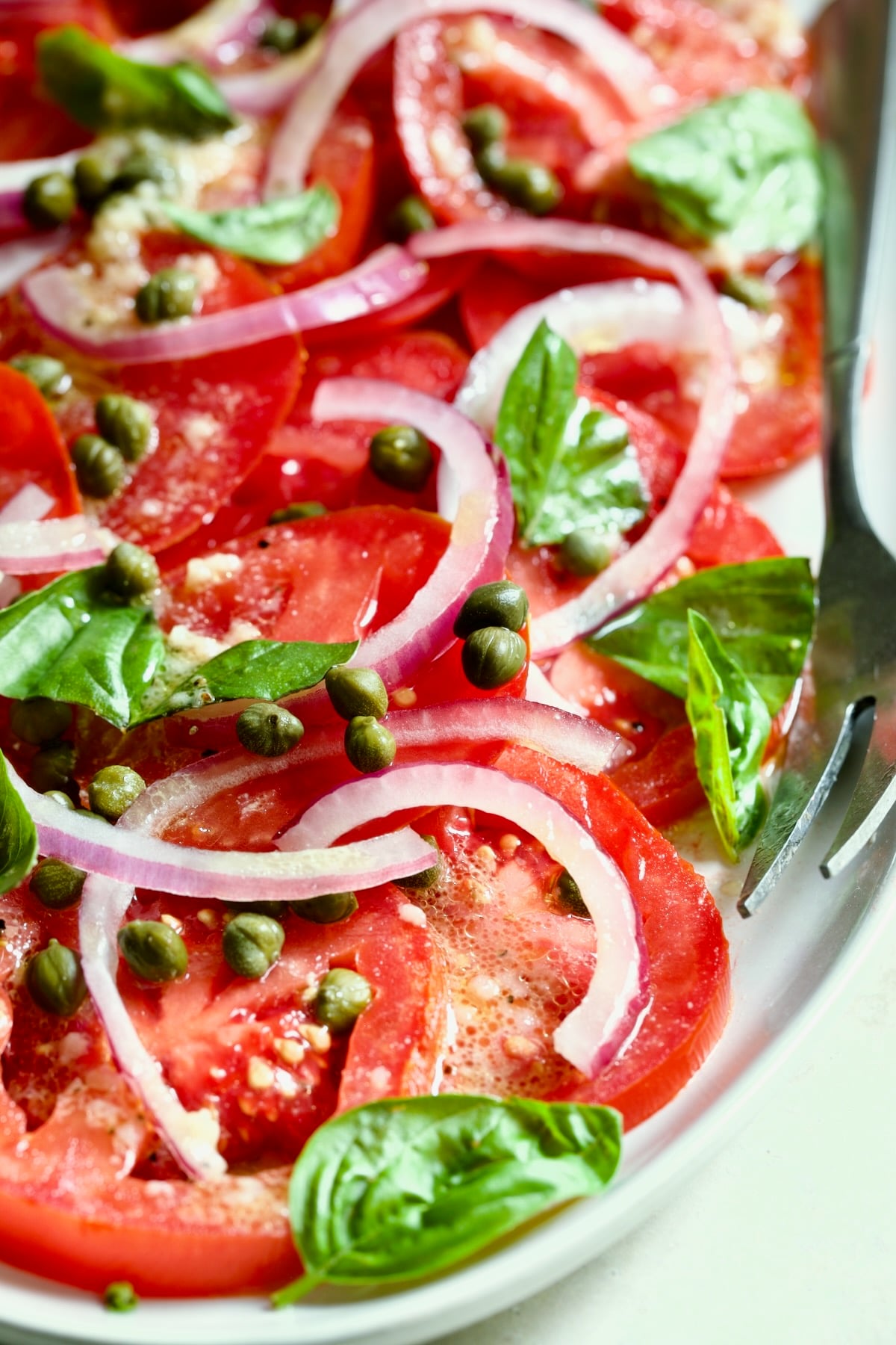 Tomato Onion Salad on white platter with serving fork.