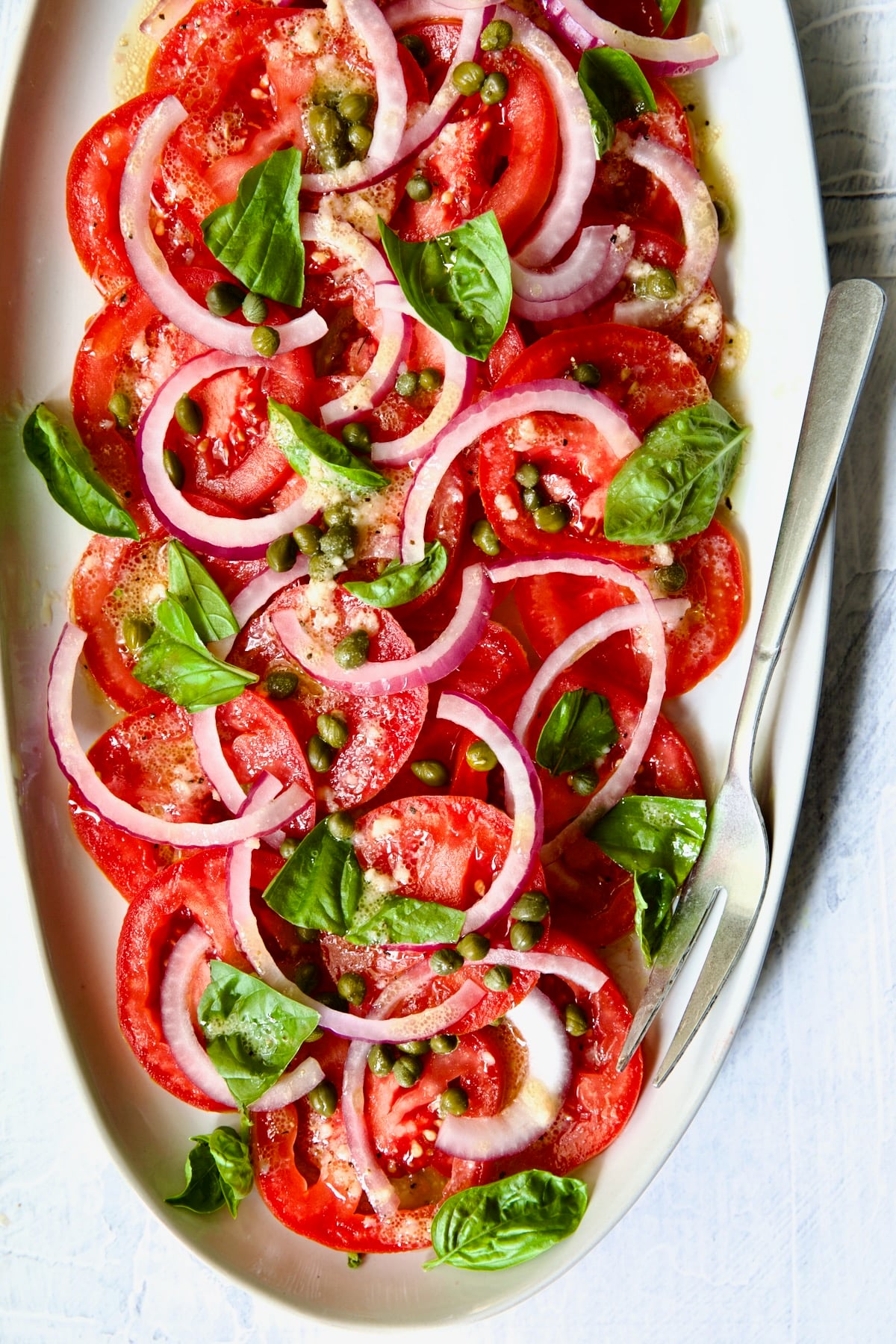 Tomato Onion Salad on white oval platter with serving fork.