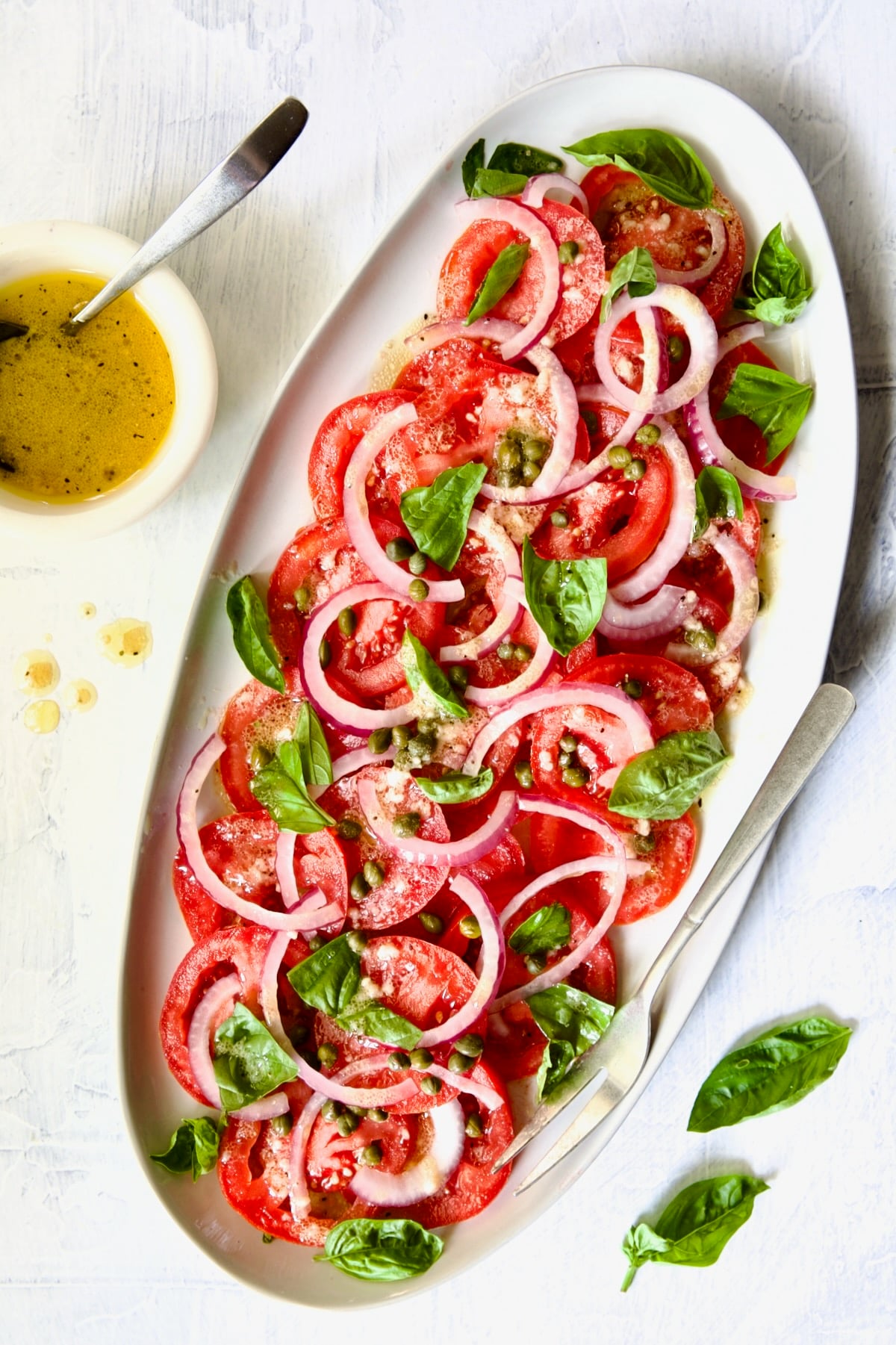 Tomato Onion Salad with vinaigrette drizzled over it garnished with fresh basil leaves.