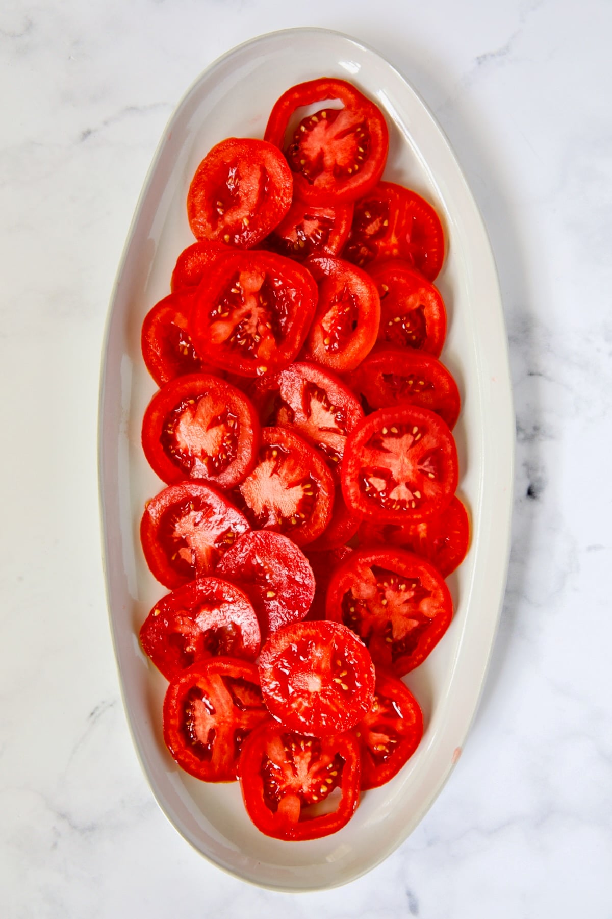 Sliced tomatoes on white oval platter.