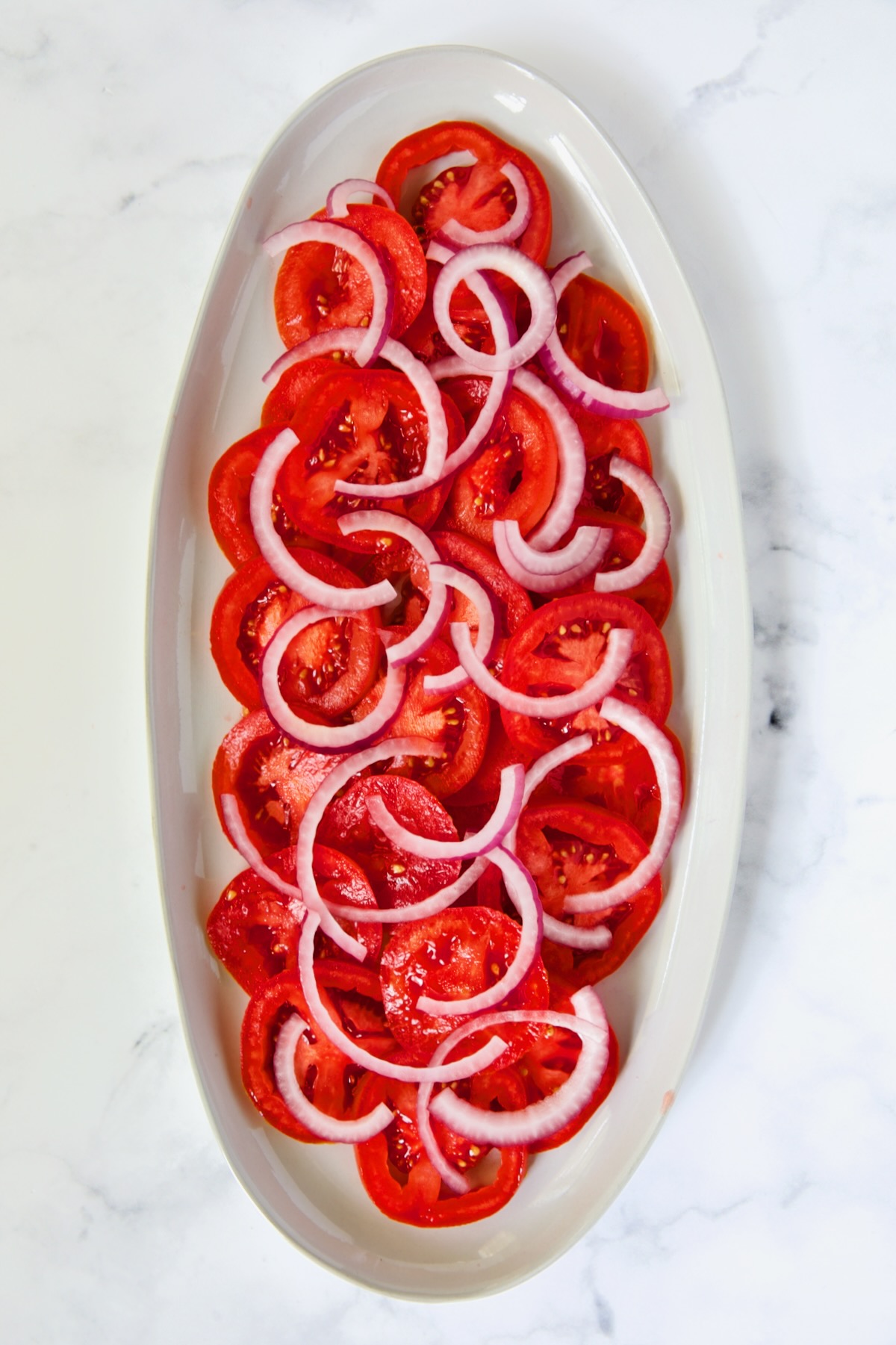 Sliced tomatoes and red onion slices on white oval platter.