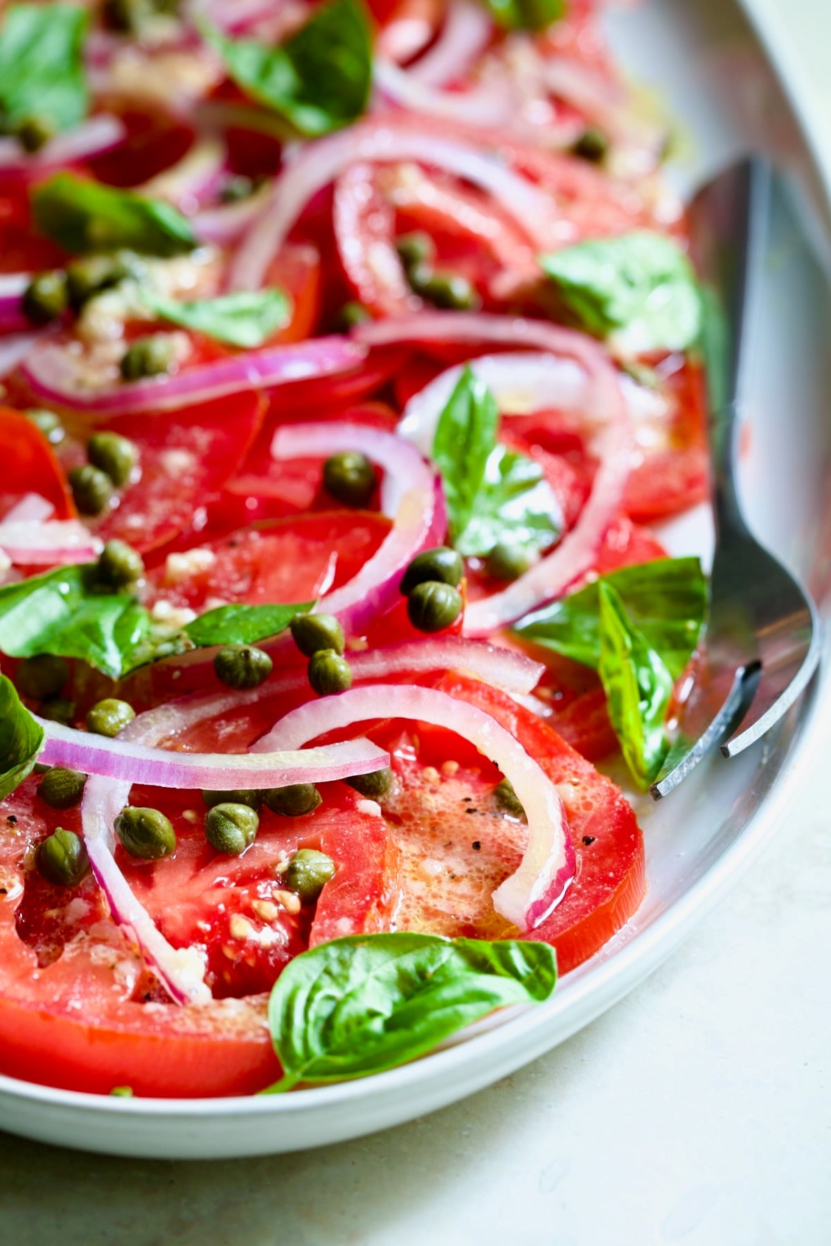 Tomato Onion Salad on white oval platter with serving fork.