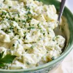 Creamy Potato Cucumber Salad in green and white serving bowl with serving spoon.