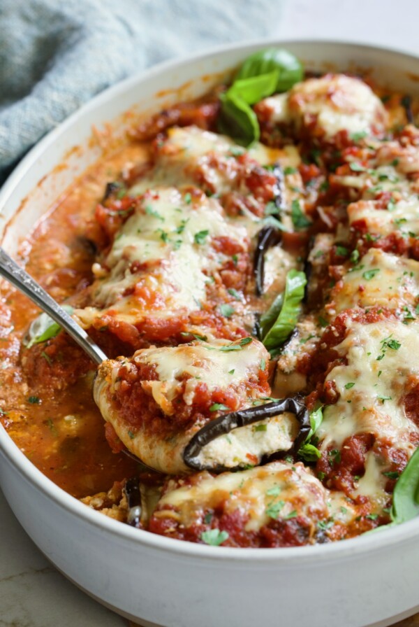 Serving spoon scooping one Eggplant Rollatini from oval baking dish.