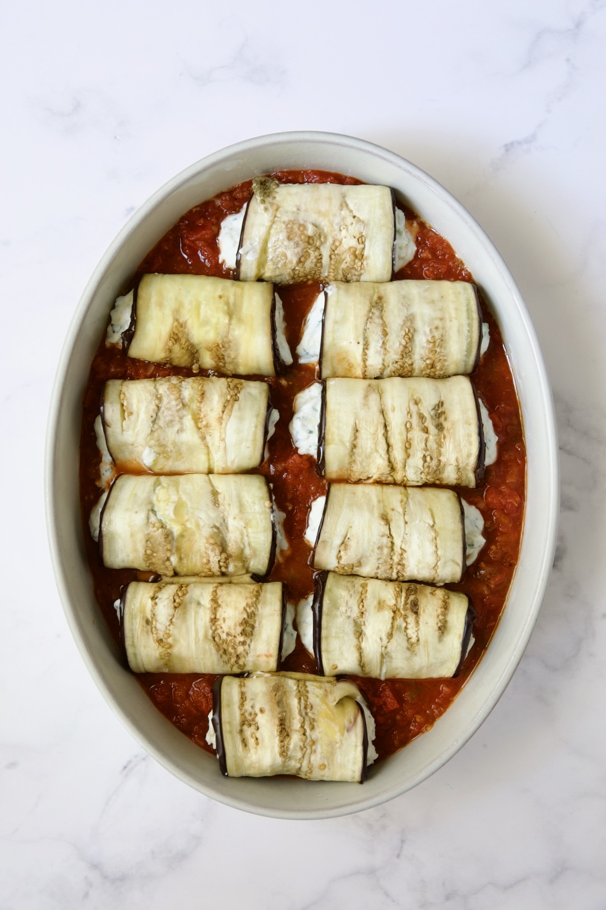 Ten eggplant slices placed on tomato sauce in oval baking dish.