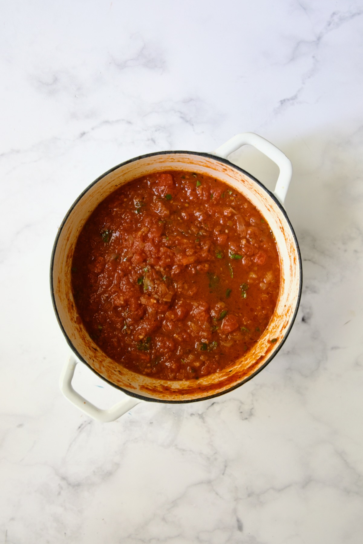 Cooked tomato sauce in white Dutch oven.