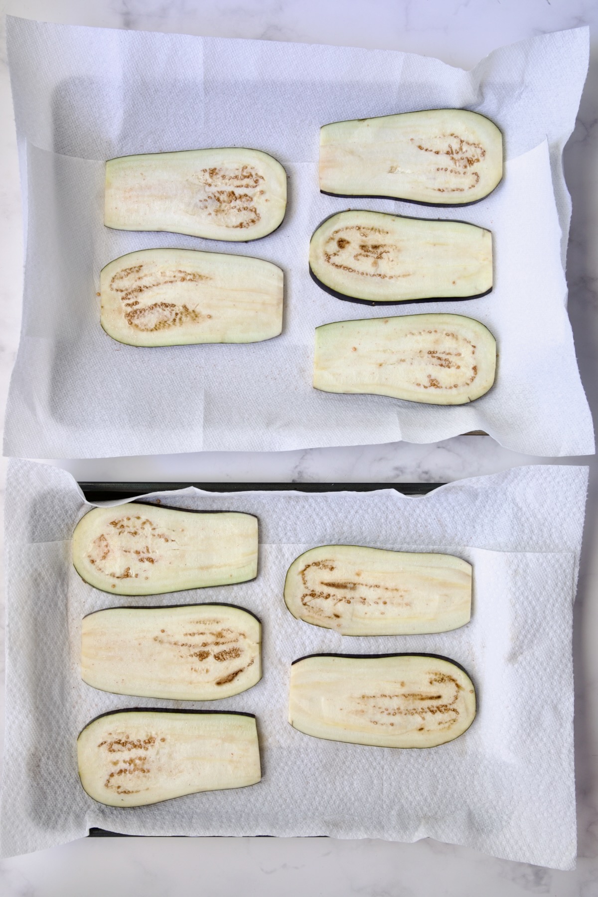 Ten eggplant slices on paper towel-lined baking sheets.
