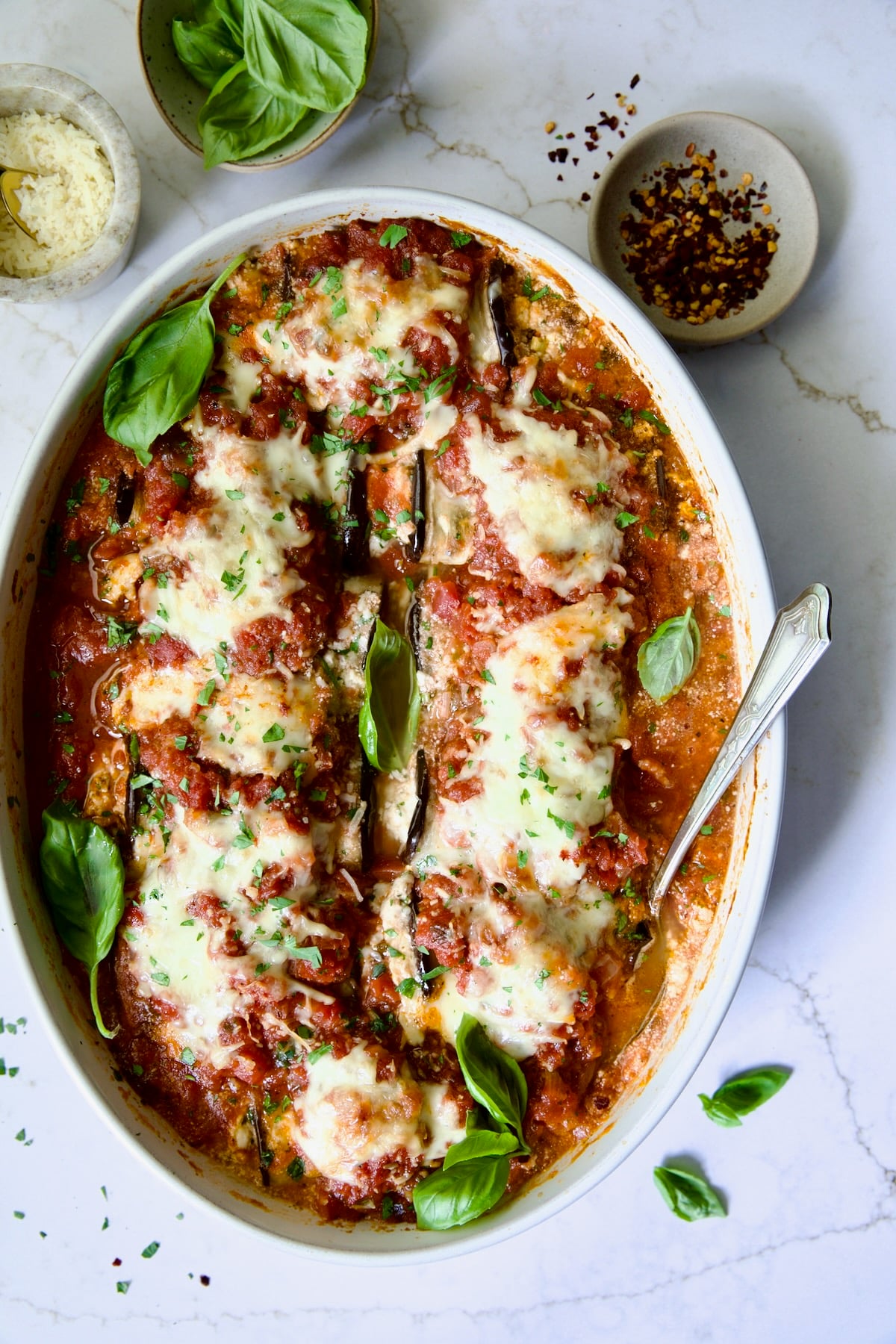 Four-Cheese Eggplant Rollatini in oval baking dish garnished with fresh basil.
