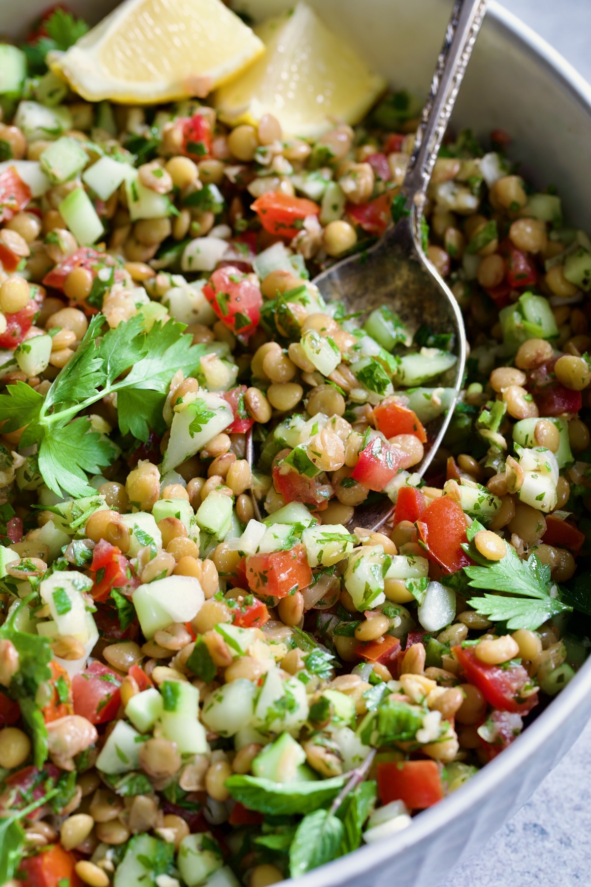 Lentil Tabbouleh in white bowl with serving spoon garnished with fresh mint sprigs and lemon wedges.