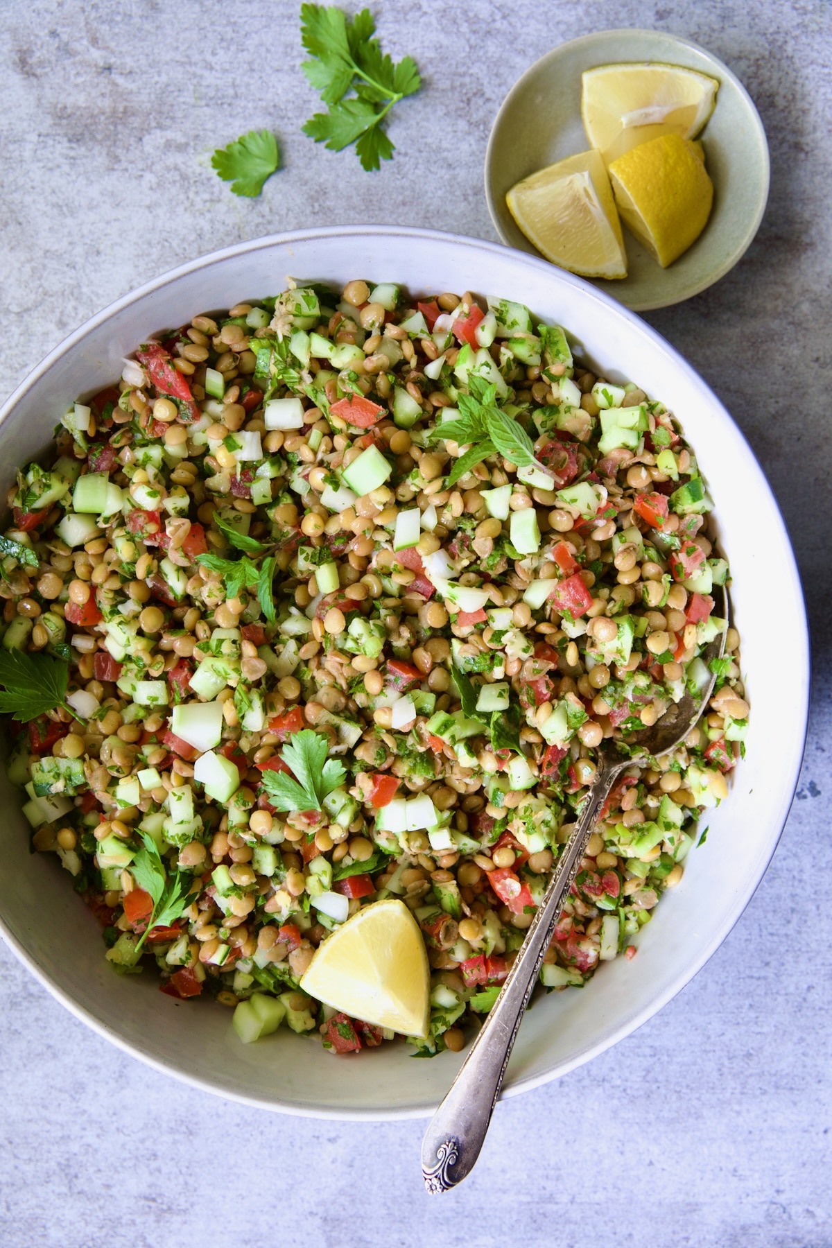 Lentil Tabbouleh in white bowl garnished with fresh mint sprigs and lemon wedges.