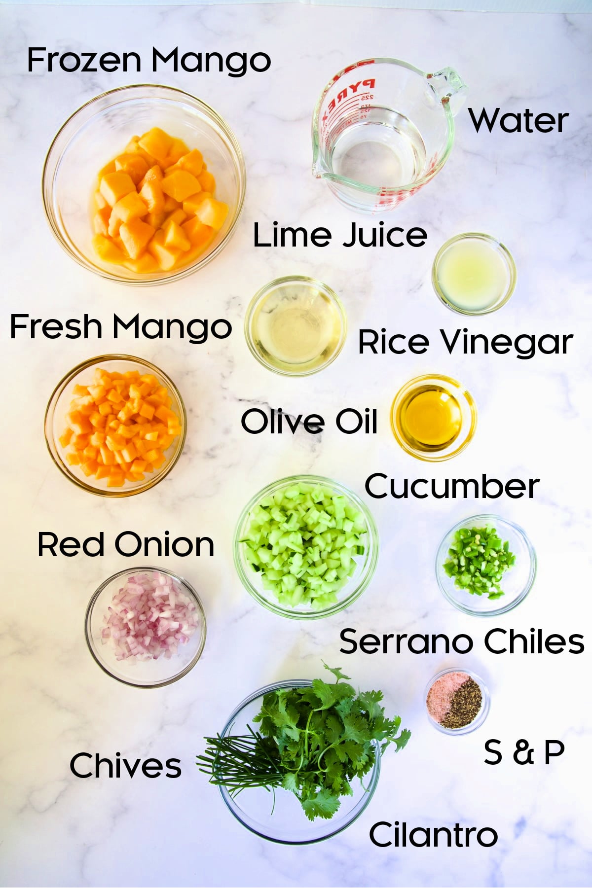 Ingredients for Mango Gazpacho in glass bowls on marble countertop.