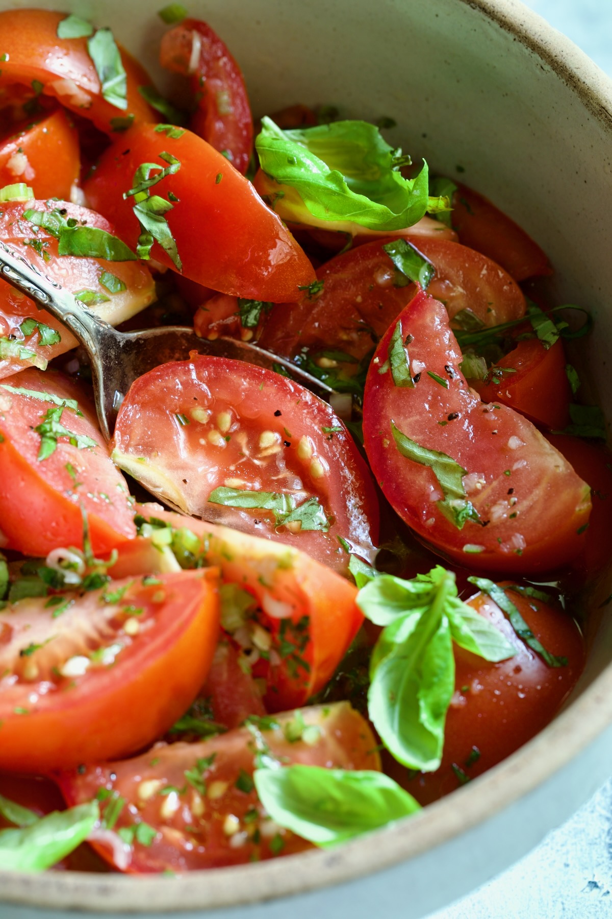 Marinated Tomatoes in old clay bowl with serving spoon garnished with fresh parsley.