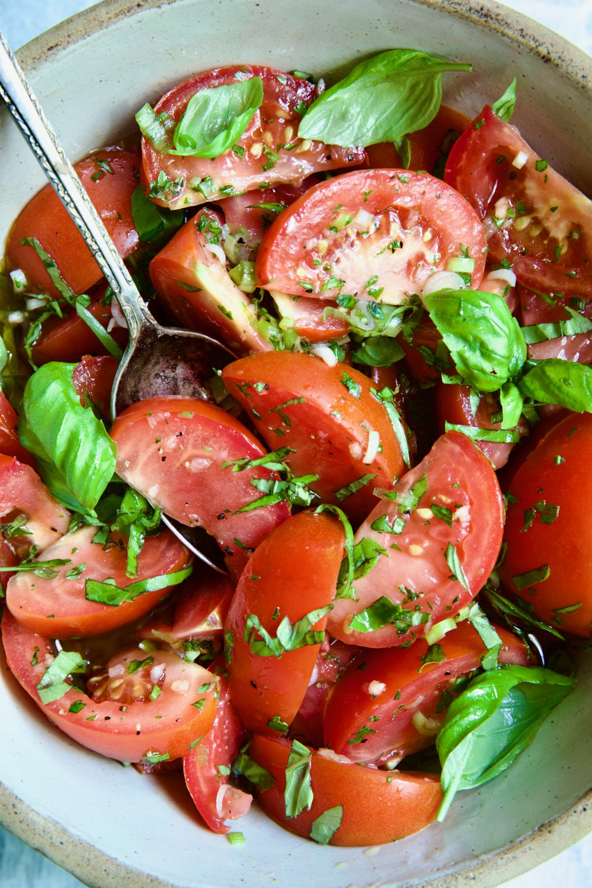Marinated Tomatoes in old clay bowl with serving spoon garnished with fresh parsley.