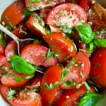 Marinated Tomatoes in old clay bowl with serving spoon garnished with fresh parsley.