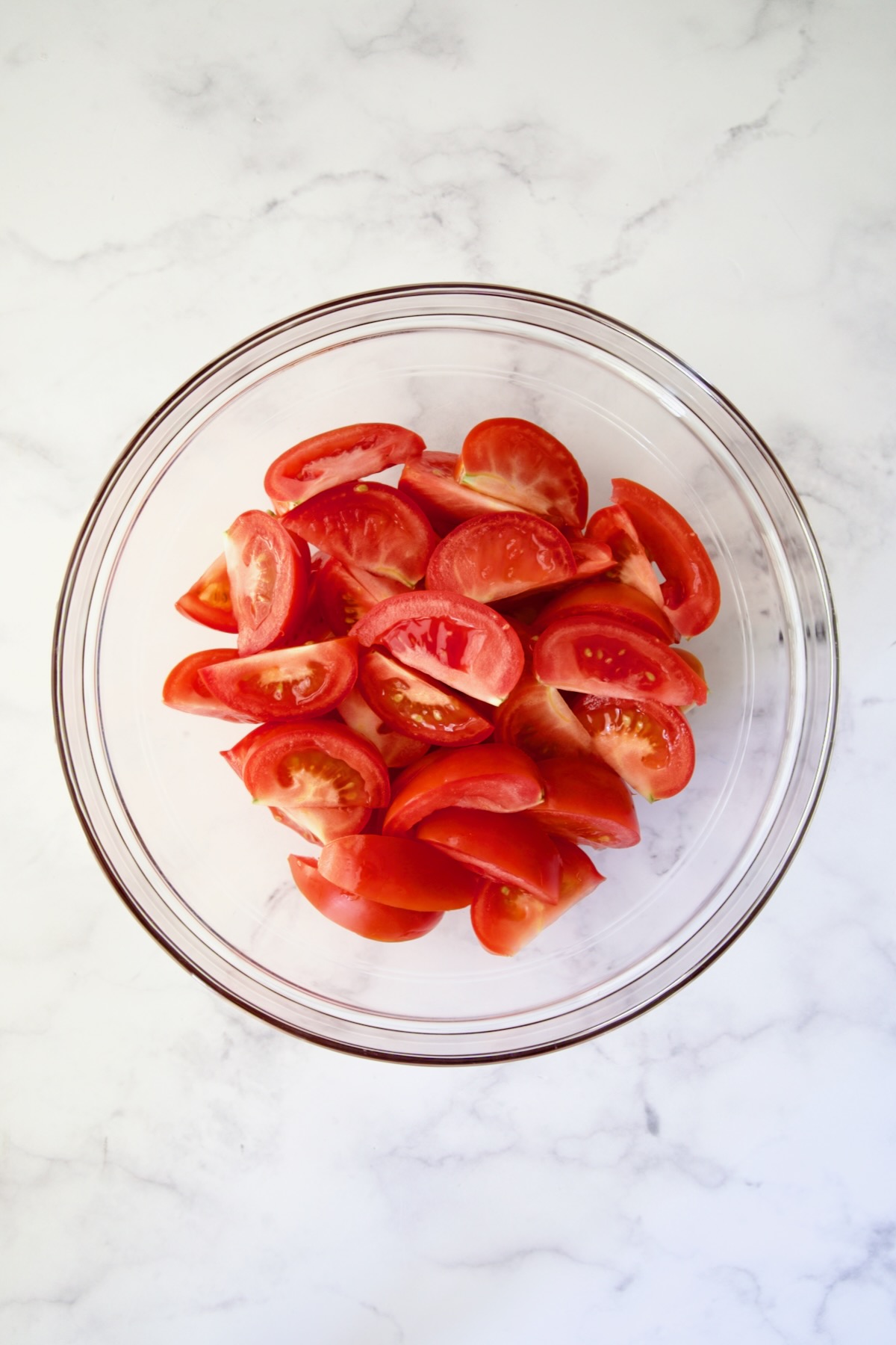 Tomato wedges in glass bowl on marble container.
