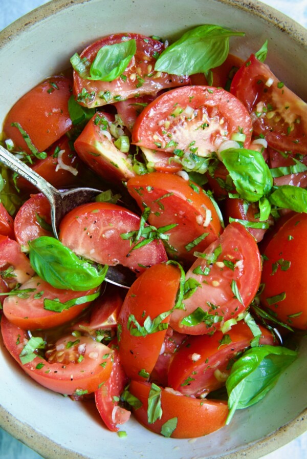 Marinated Tomatoes in old clay bowl with serving spoon garnished with fresh parsley.